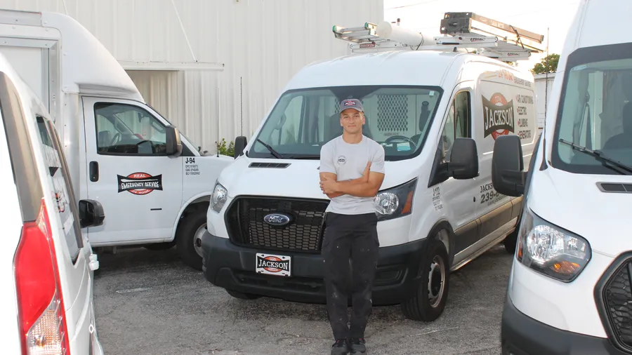 Jackson Total Service technician standing with the lettered service vans in Naples